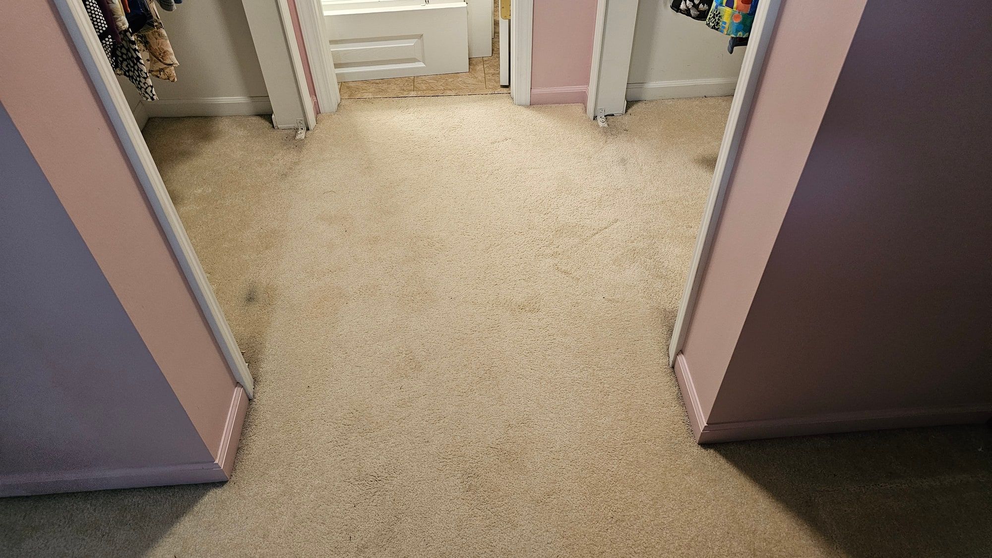 A hallway carpeted in pale beige, matted and darkened down the middle where everyone walks, bedroom doors standing open either side.