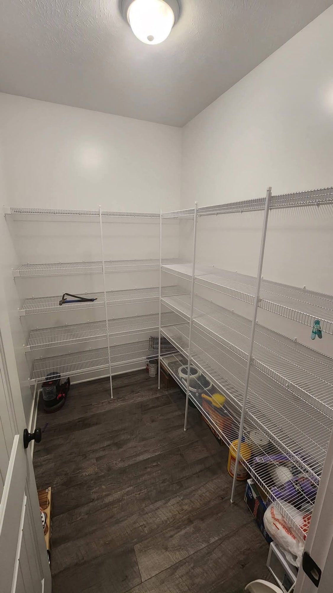 A walk-in pantry fitted with white wire shelving on three walls, tins and boxes stacked on the floor underneath.