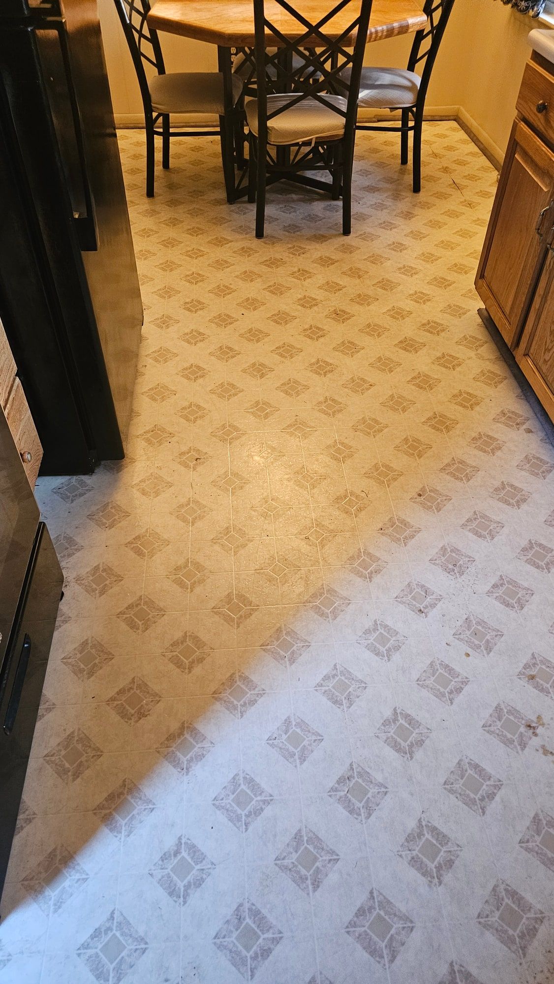 A kitchen floor in sheet vinyl printed with a beige diamond pattern, rubbed pale along the line between the table and the counter.